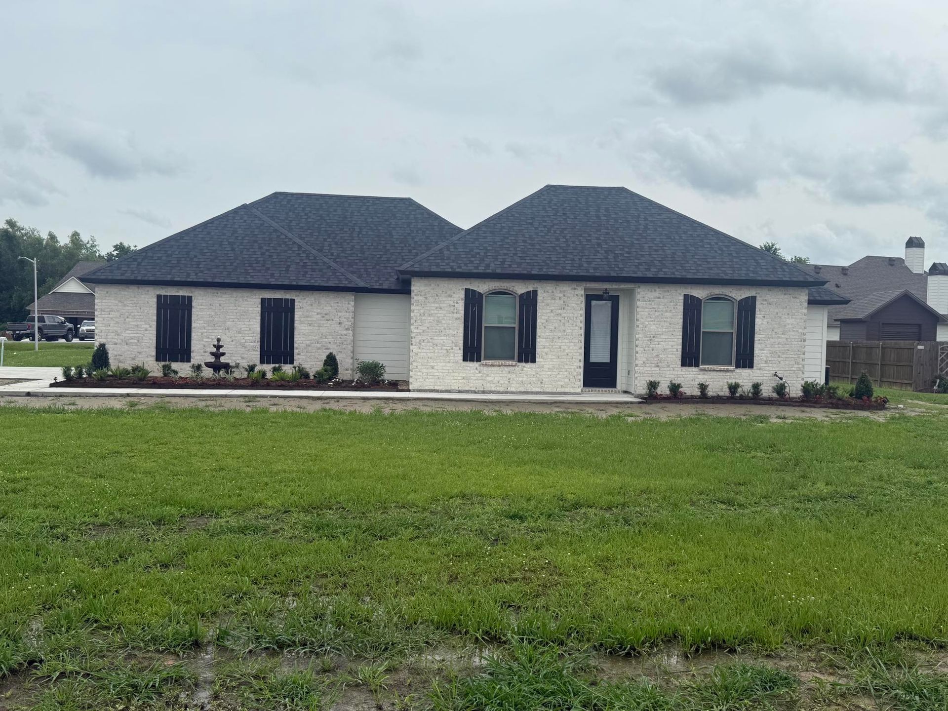 White brick house with black shutters, dark roof, and green lawn.