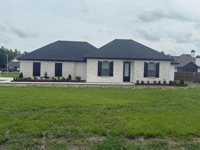 White brick house with black shutters, dark roof, and green lawn.