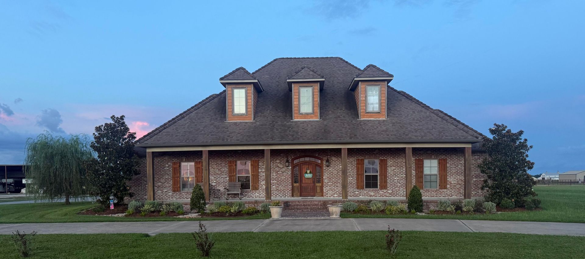 A large brick house with a long porch under a blue and pink sky.