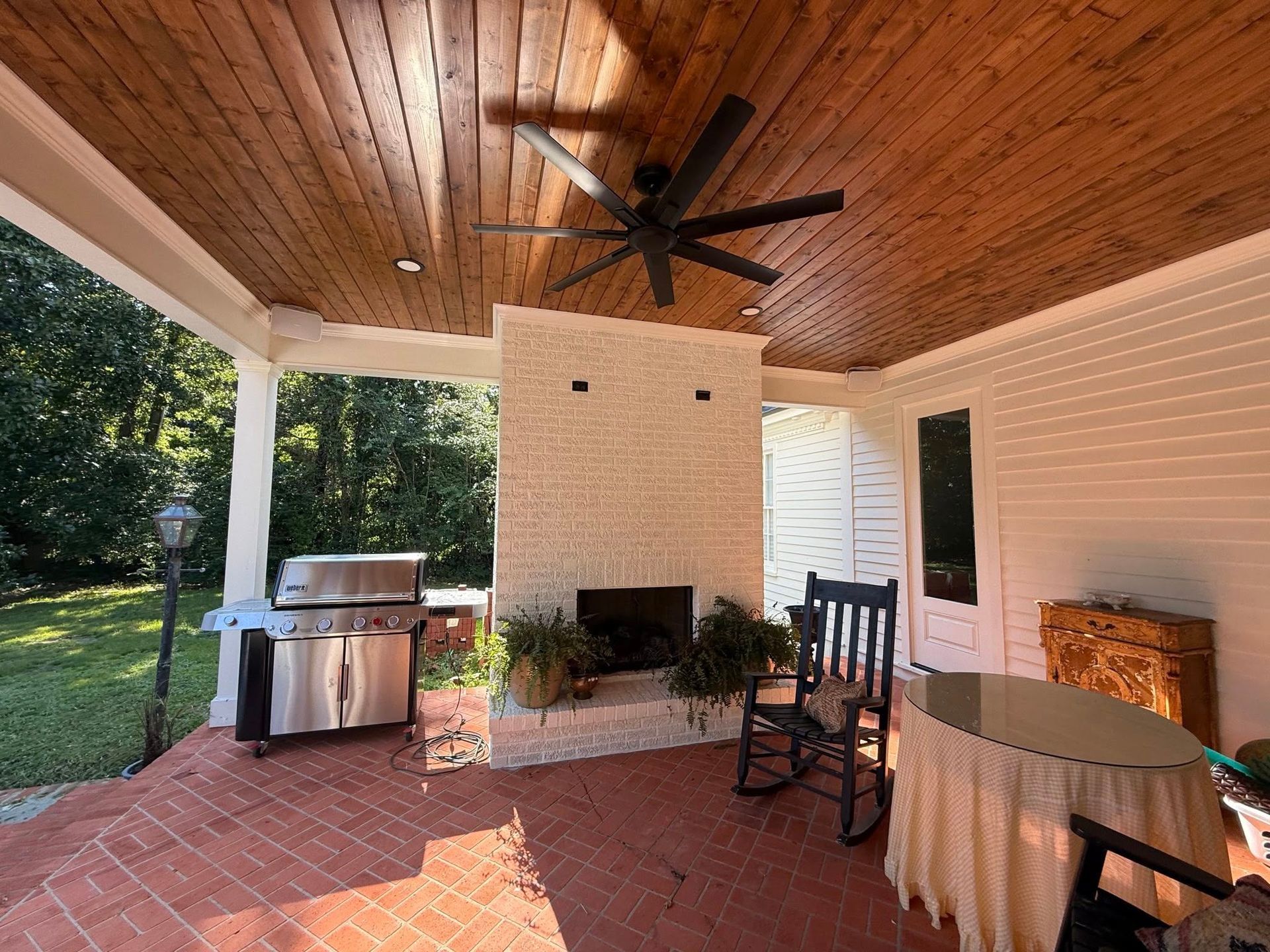 Covered outdoor patio with brick floor, fireplace, grill, and ceiling fan.