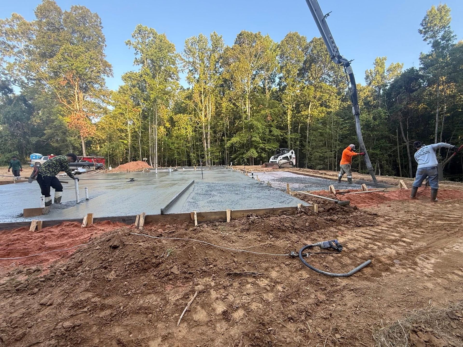 Construction workers pouring concrete for a foundation, using a pump truck and hand tools outdoors.