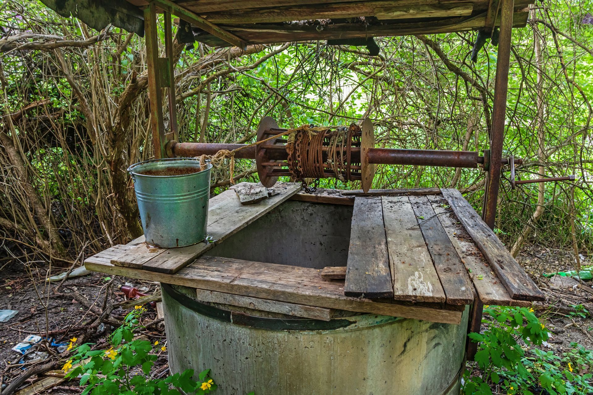 An old well with a bucket on top of it in the woods. An old well with a bucket on top of it in the woods.
