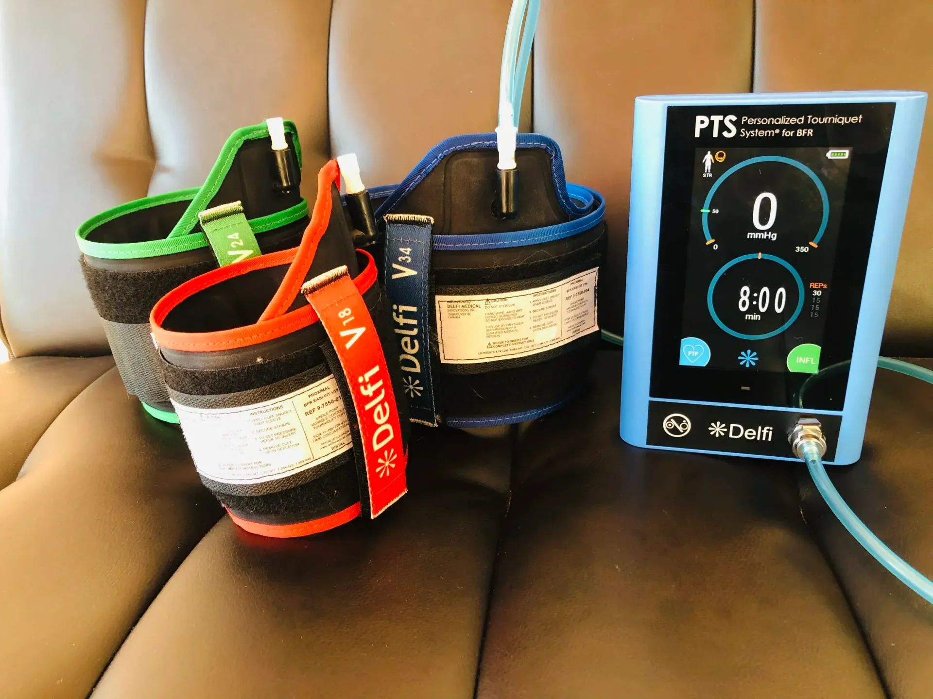 Three cuff-like medical devices (red, green, and blue) with a blue display device on a dark surface.