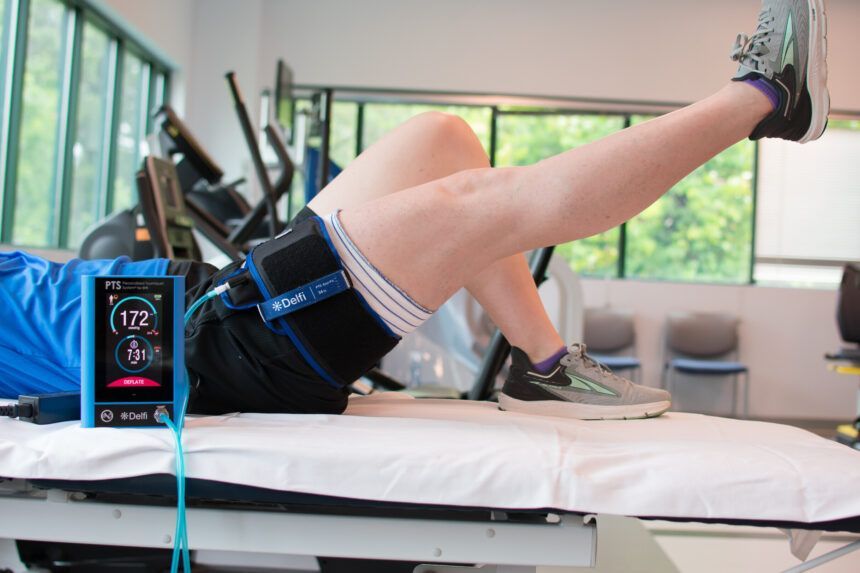 Person doing exercise with leg lift, device measuring vitals, in a clinic.