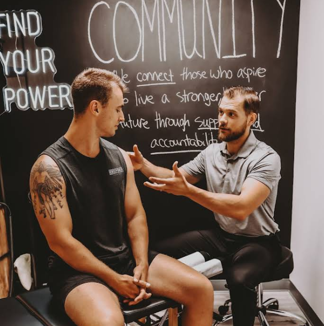 Man with arm injury consults with a healthcare professional in front of a chalkboard with