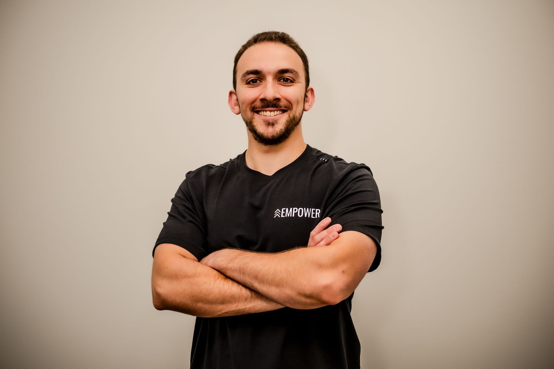 Man with short brown hair and beard smiles in front of a dark wood background, wearing a gray t-shirt.