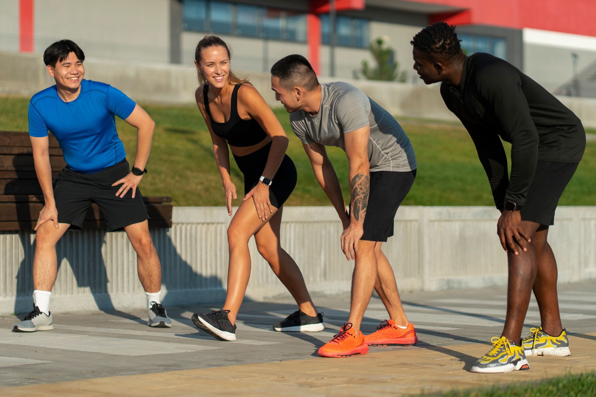 Four diverse people stretch their legs outdoors, preparing to exercise.