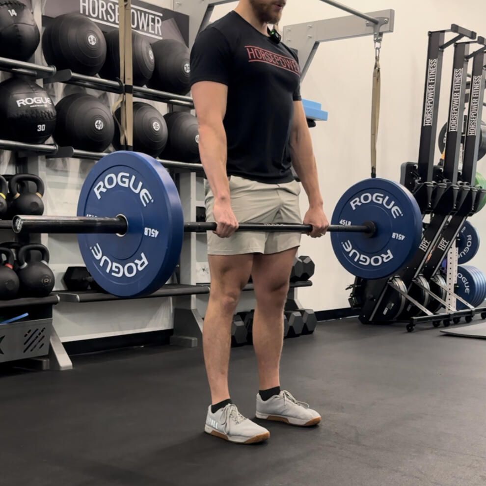 Man performing a deadlift in a gym. He's holding a barbell with blue weight plates.