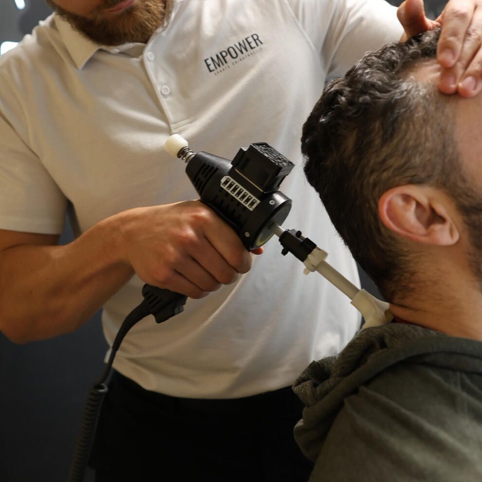 Therapist using a medical device on a patient's neck in a clinical setting.
