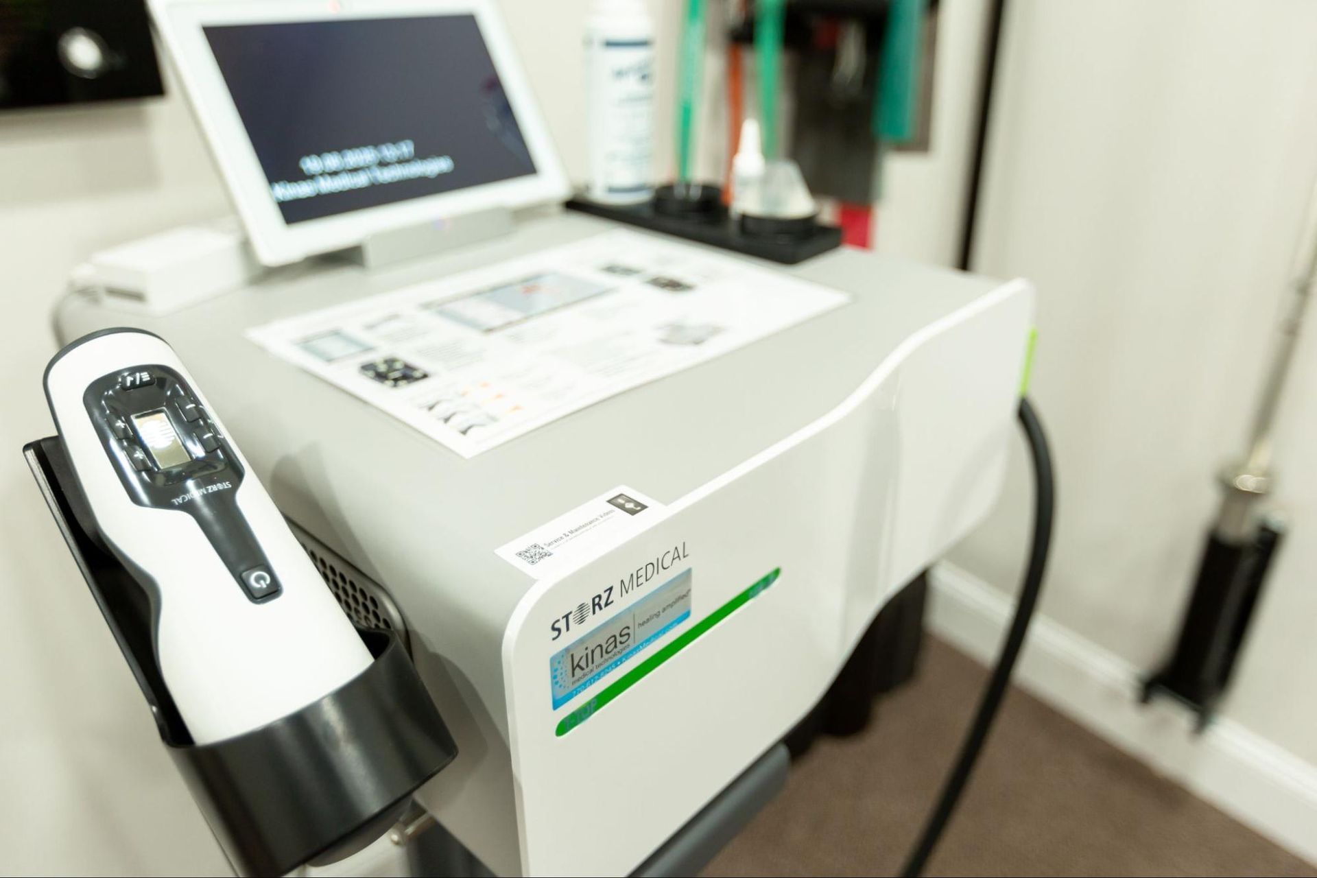 Medical device with tablet display and hand piece, likely used in a clinic.