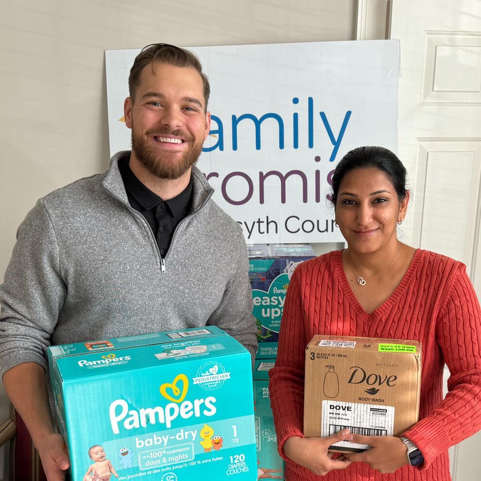Two people smiling, holding donations for Family Promise. One holds diapers, the other toiletries.