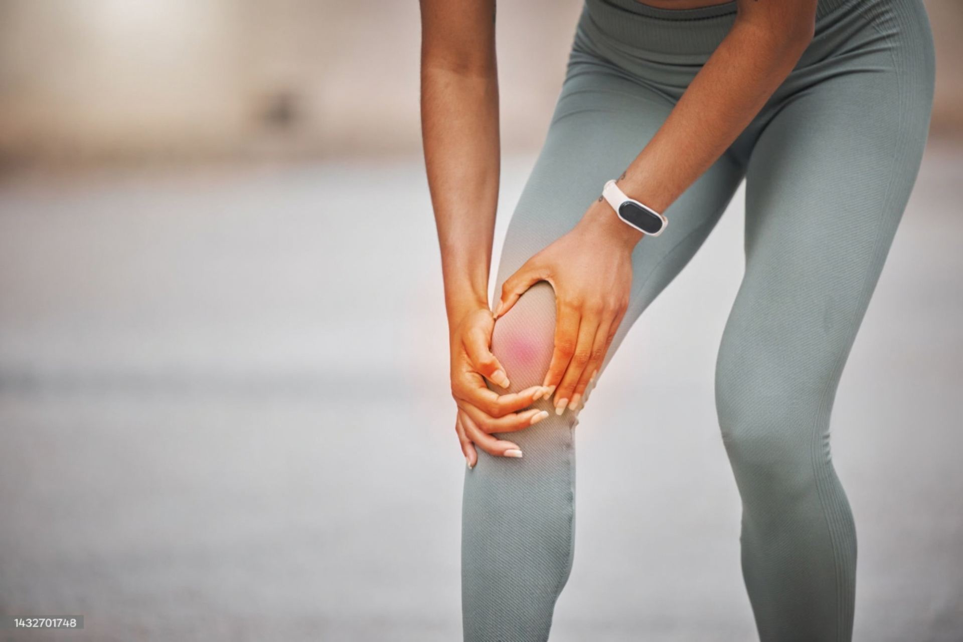 Woman holding her knee in pain, highlighting a possible injury. She is wearing grey leggings and has a smartwatch on.