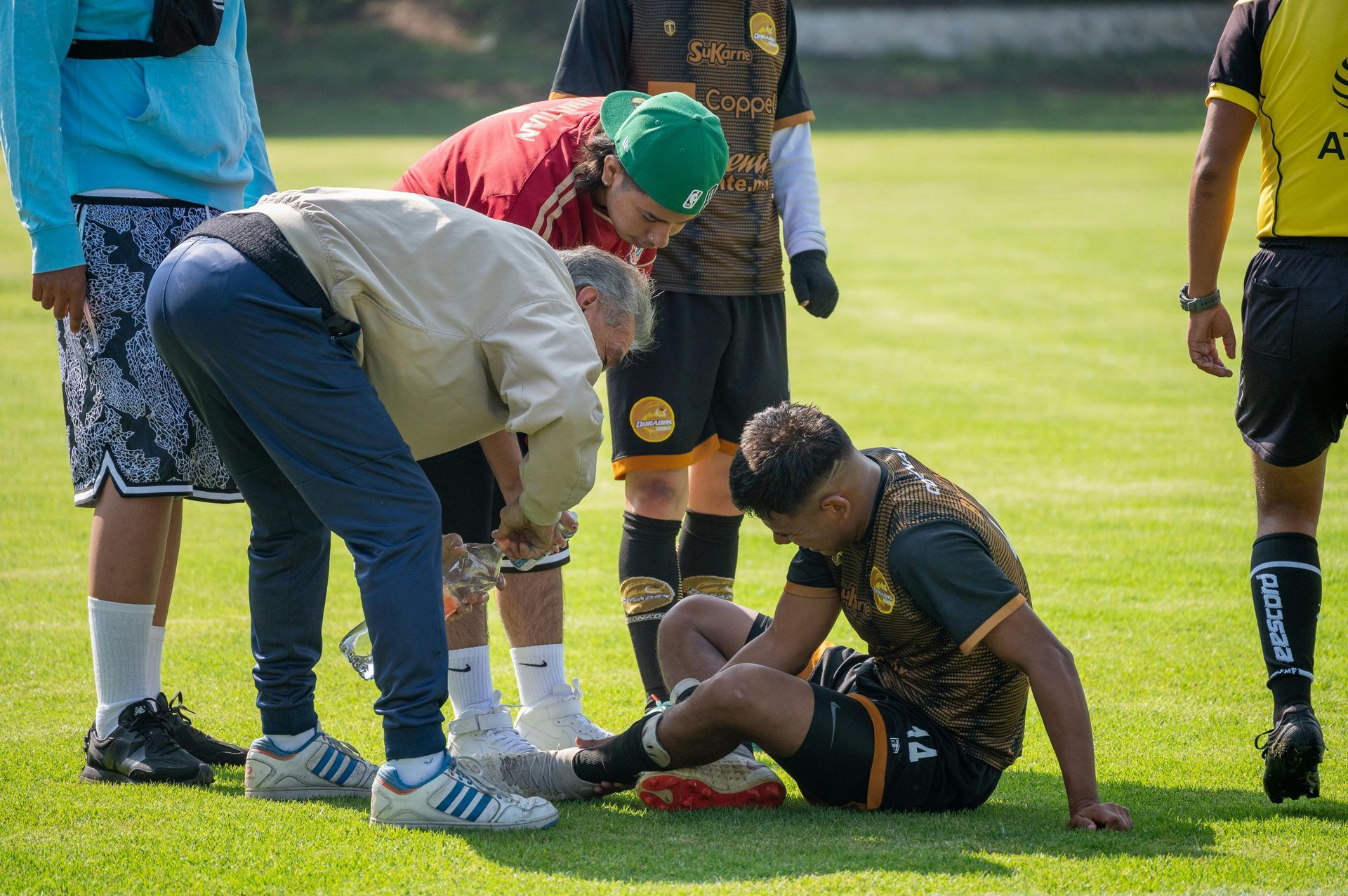 Soccer player injured on field, being attended to by staff and referee.