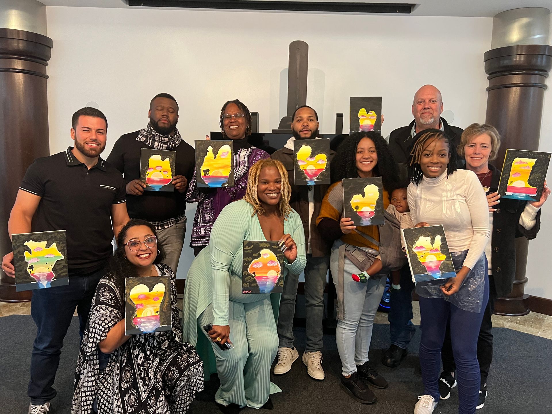 A group of people are posing for a picture while holding paintings.