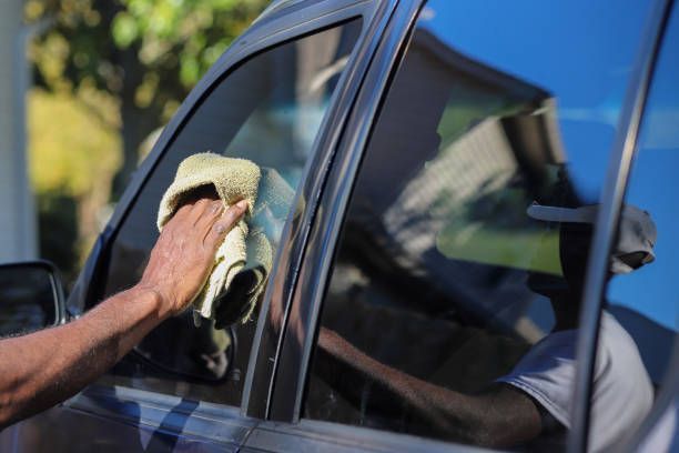 A man is cleaning a car window with a towel.