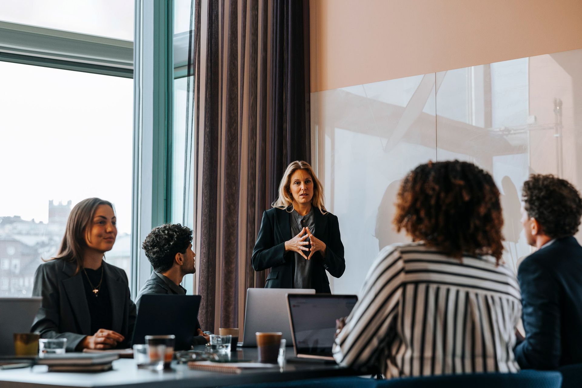 Woman giving presentation to colleagues in a modern office with city view.
