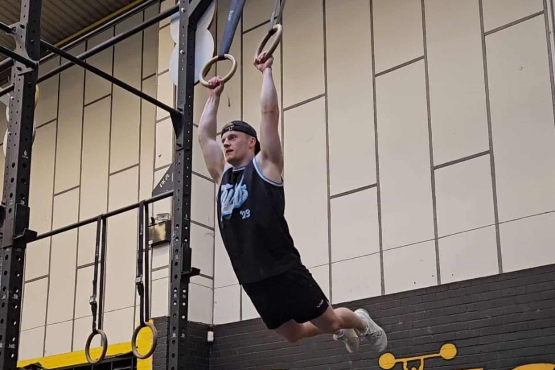 A man is doing a pull up on gymnastic rings in a gym.