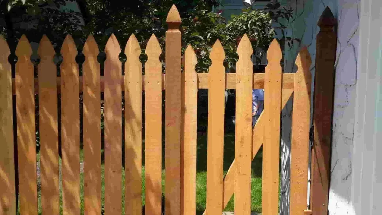 A wooden picket fence with a gate in front of a house.