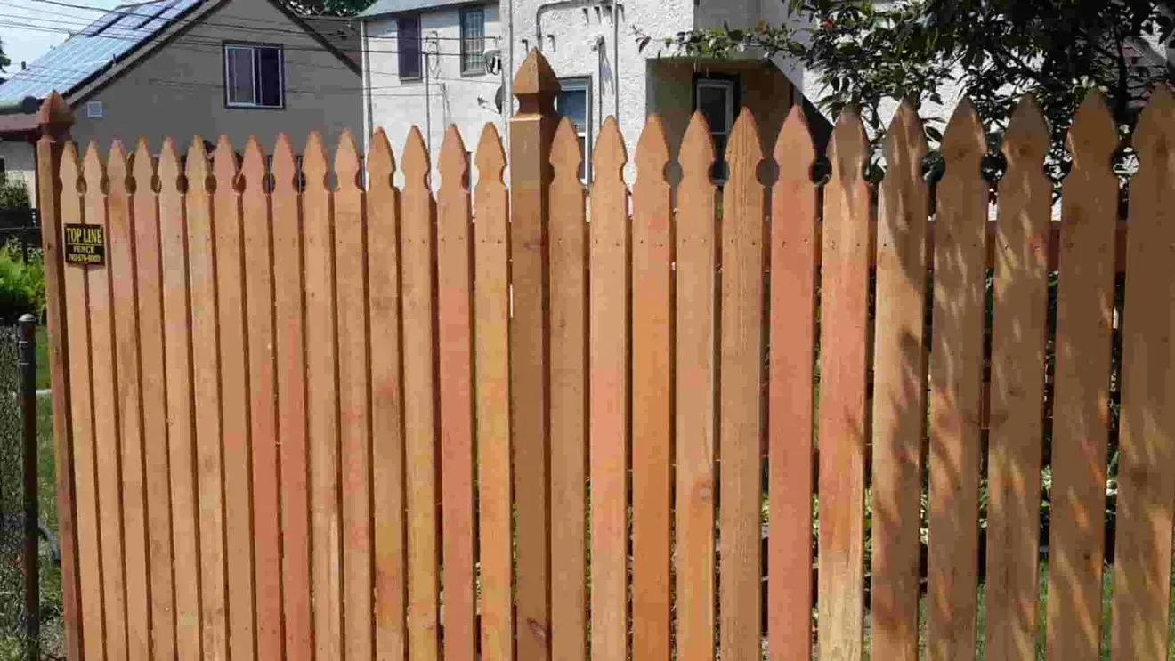 A wooden picket fence with a gate in front of a house.