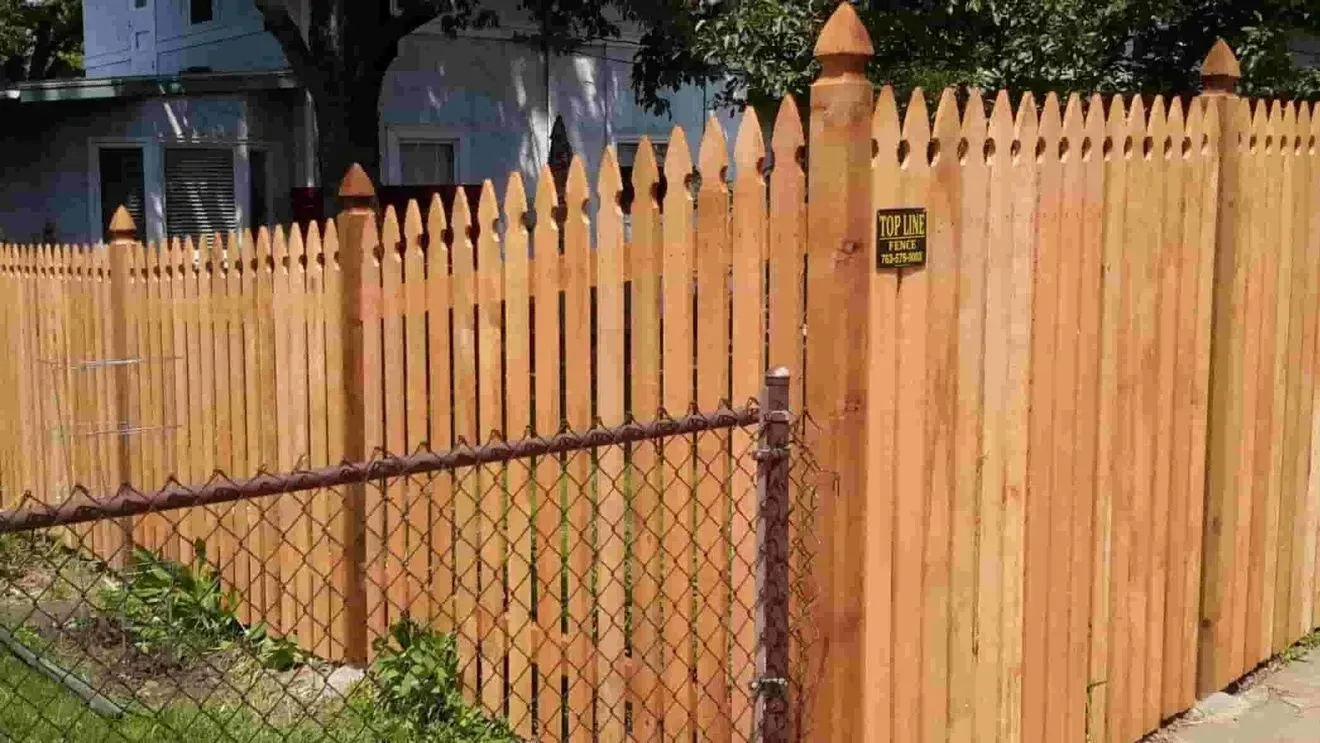 A wooden picket fence with a chain link fence in front of a house.
