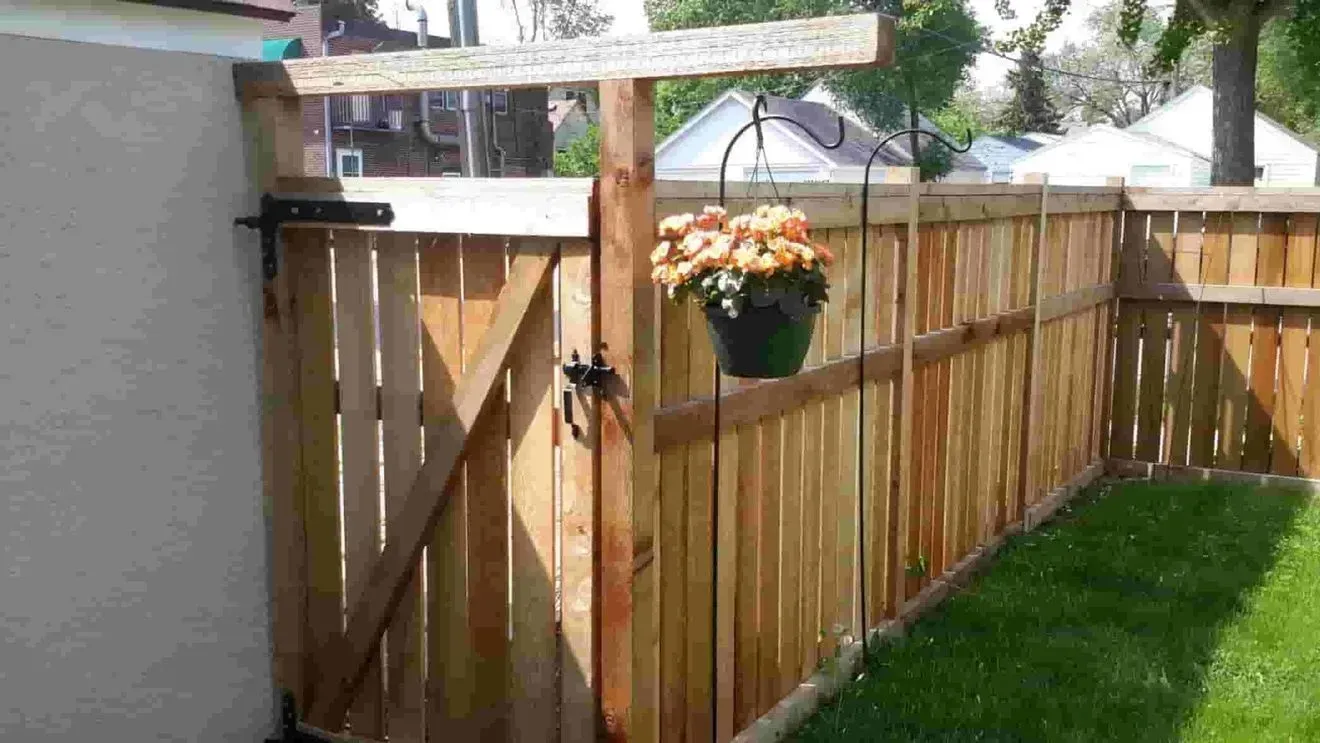 A wooden fence with a gate and a potted plant hanging from it.