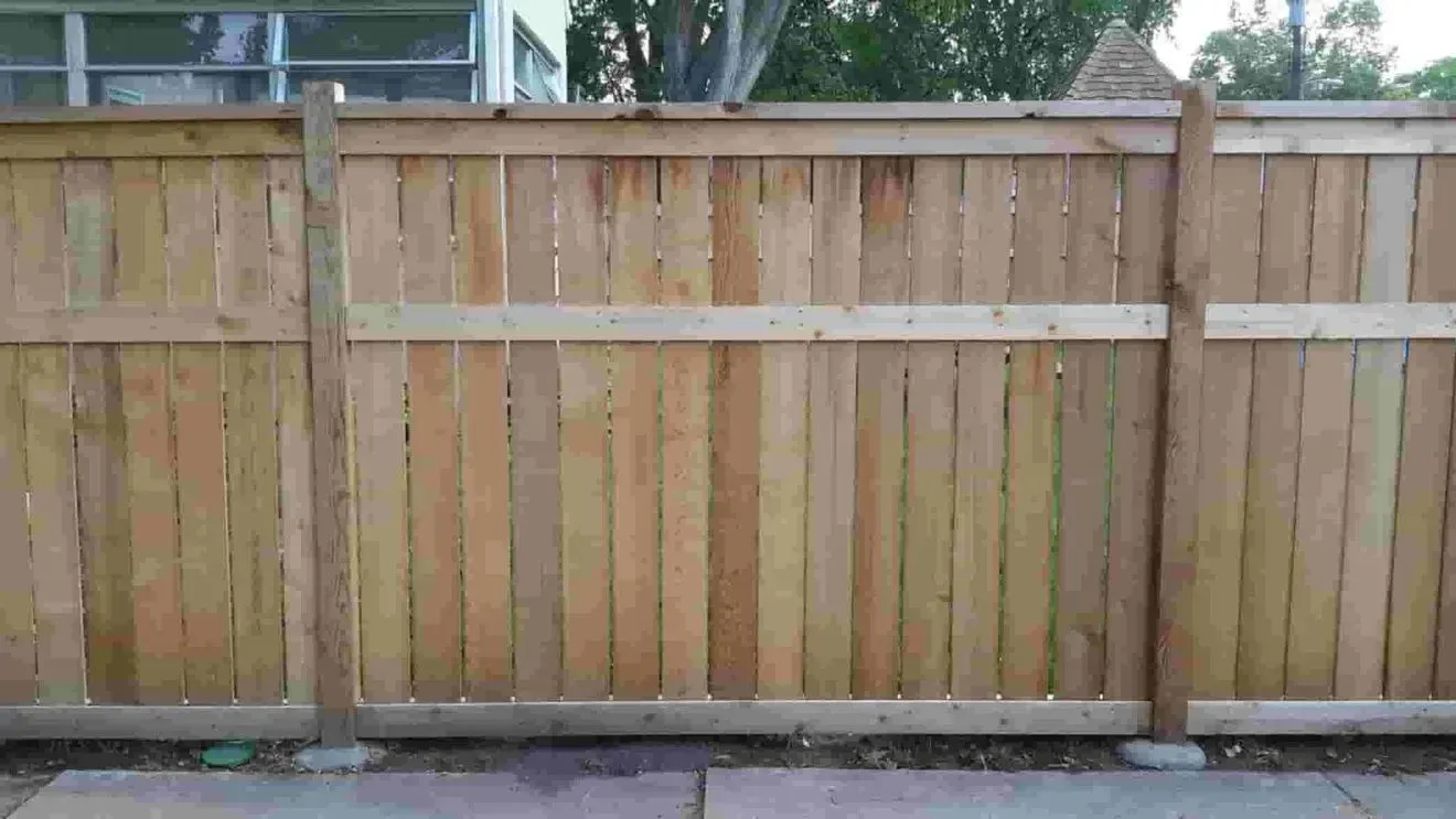 A wooden fence is sitting on a sidewalk in front of a house.