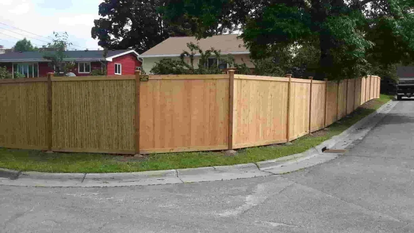 A wooden fence is sitting on the corner of a street.