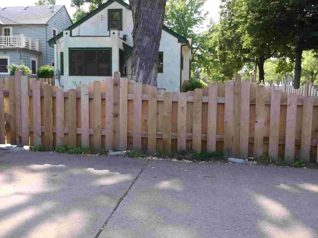 A wooden fence surrounds a driveway in front of a house