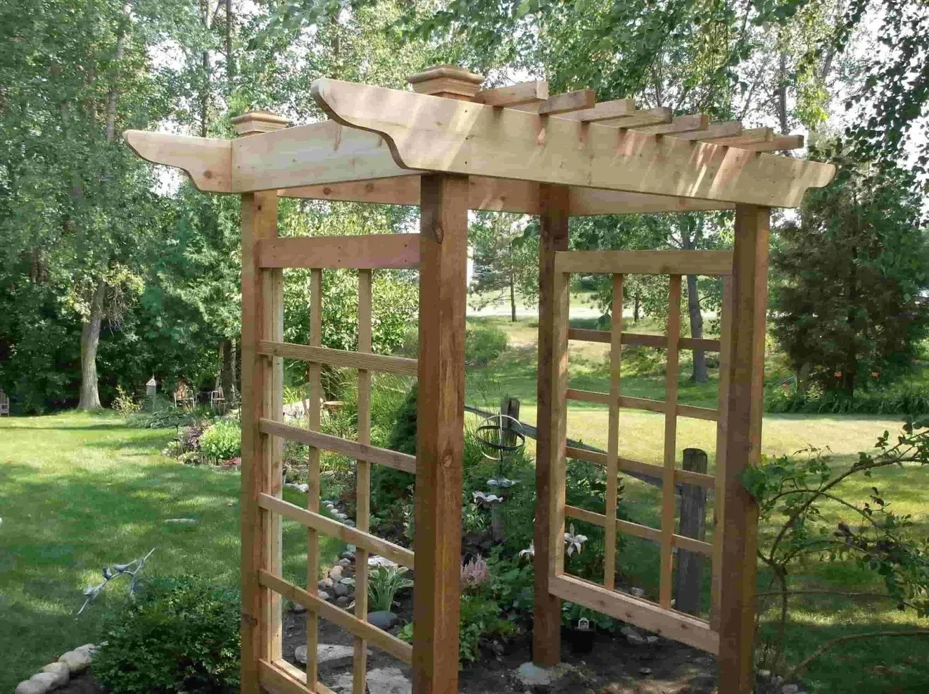 A wooden pergola is sitting in the middle of a lush green garden.