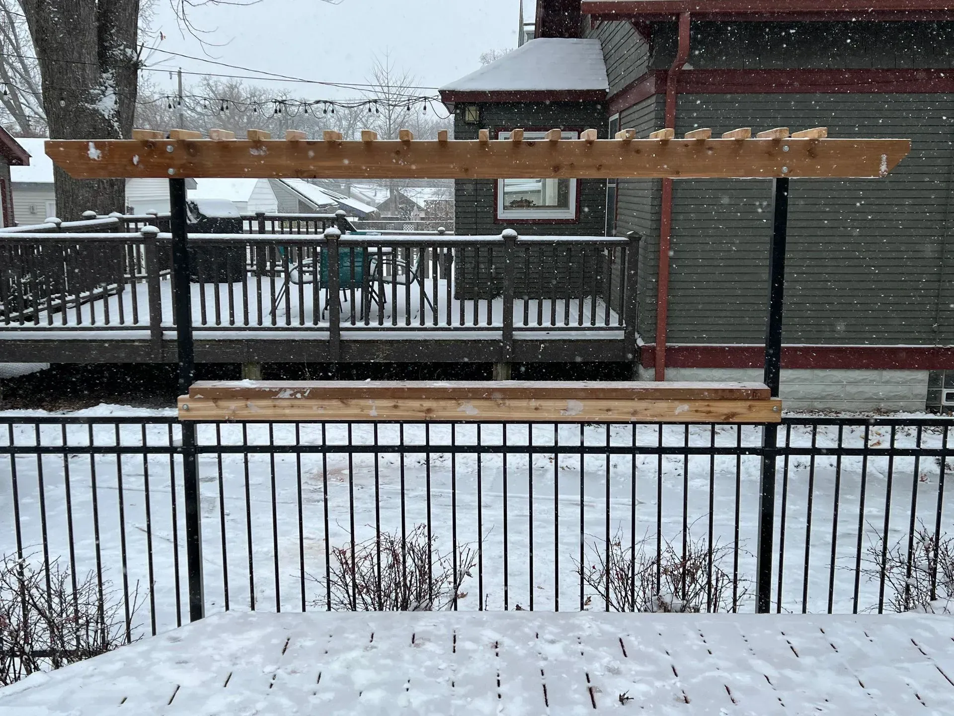 A snowy deck with a pergola and a fence