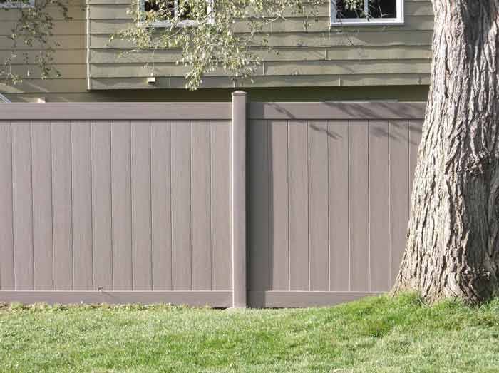 A wooden fence surrounds a lush green lawn in front of a house.
