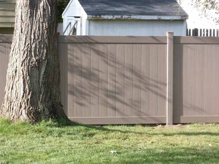 A brown wooden fence with a tree in front of it.