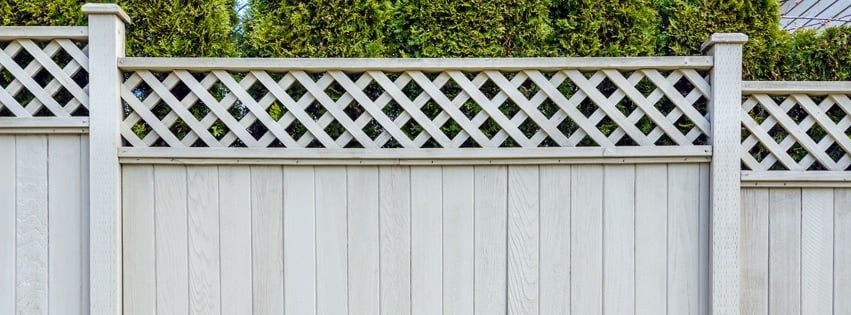 A white wooden fence with a lattice design is surrounded by trees.