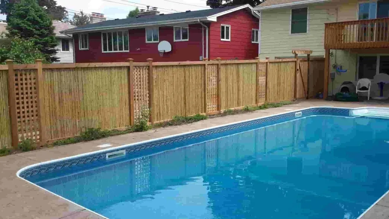 A large swimming pool surrounded by a wooden fence in front of a house.