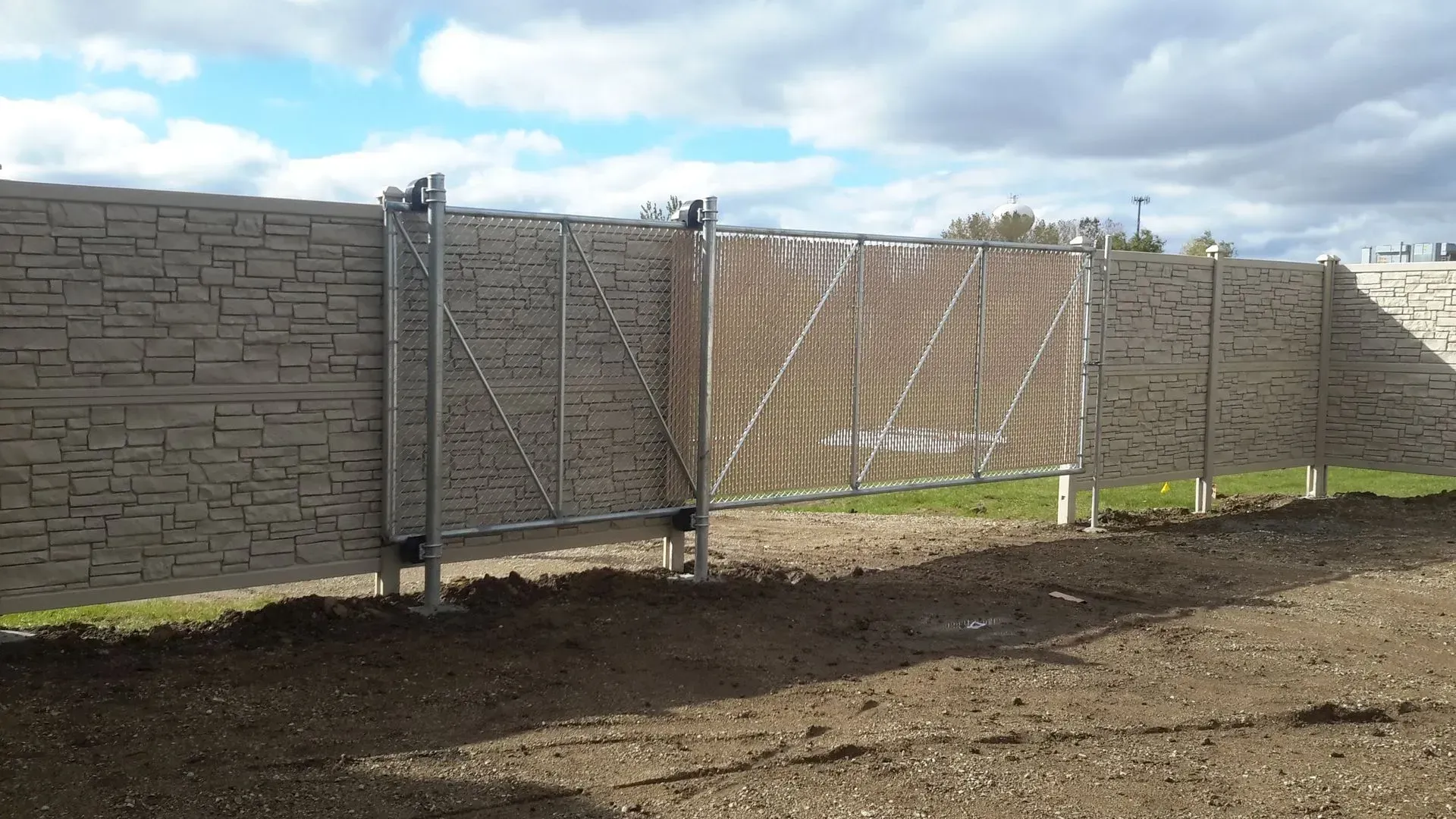 A brick fence with a metal gate in the middle of a dirt field.