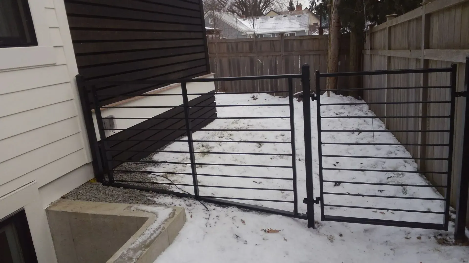 A black gate is sitting in the snow in front of a house.