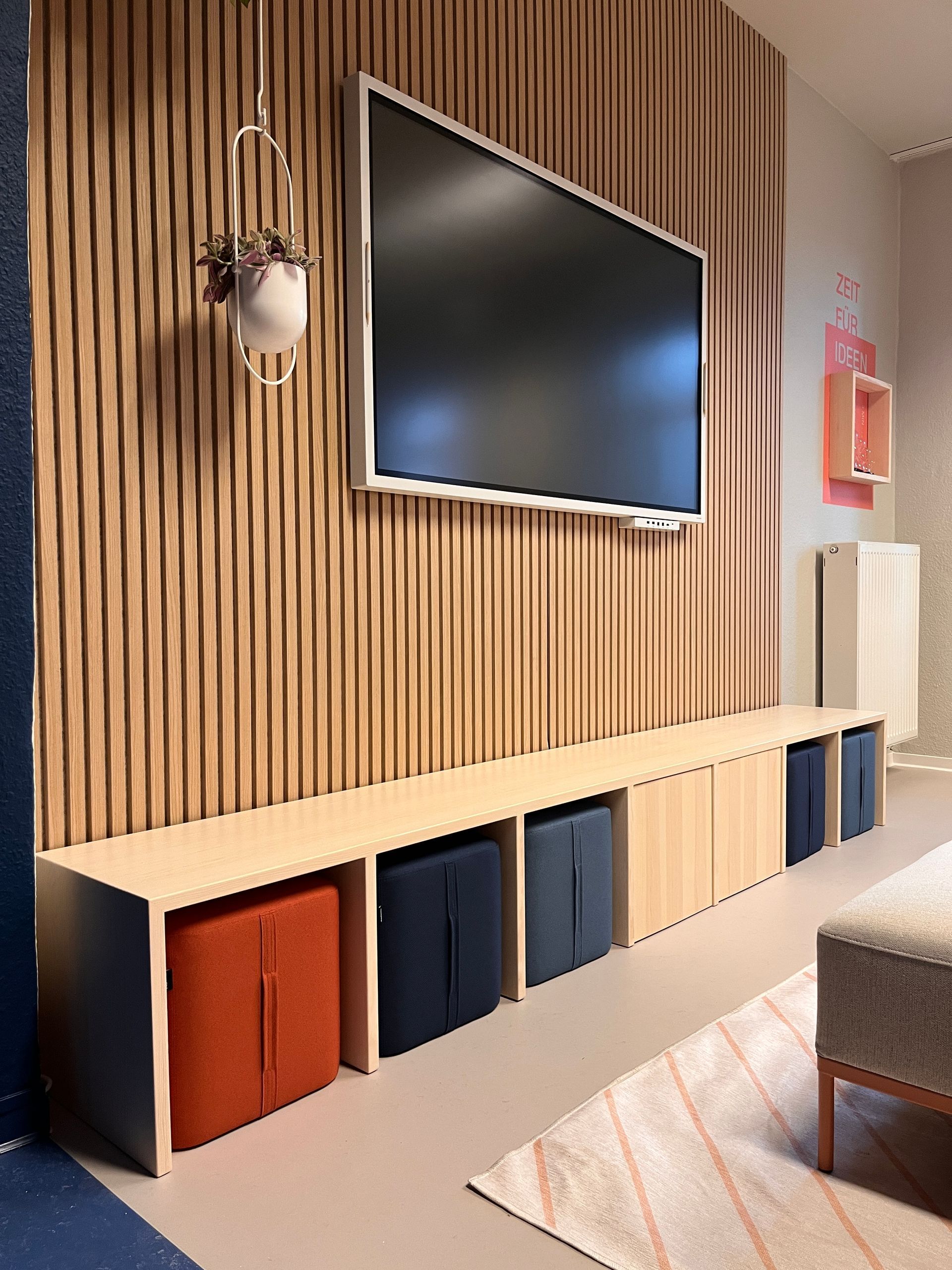 Wandverkleidung Akustikpaneele in Eiche auf schwarzem Vlies mit Blumenampel. Sitzbank aus Massivholz Kiefer mit Sitzhockern.