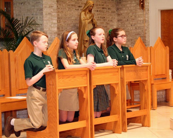 A group of children are kneeling in front of a statue of jesus