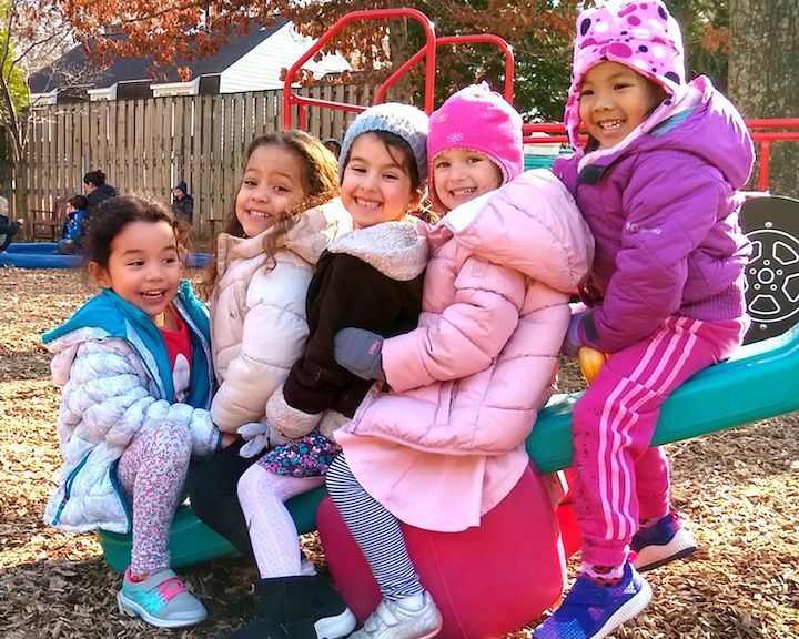 A group of young girls are sitting on a seesaw at a playground.