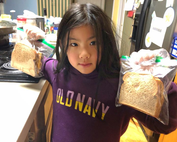 A little girl wearing an old navy shirt is holding two slices of bread