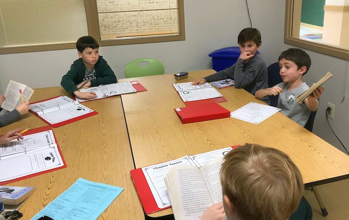 A group of children are sitting around a table reading books