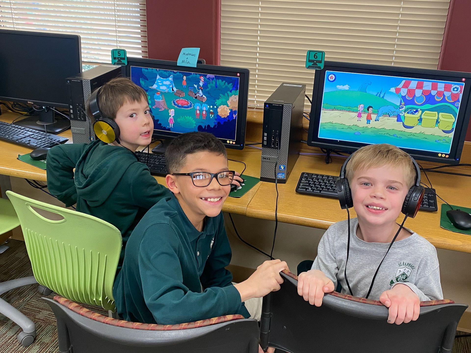 Two boys are looking at a computer screen and one of them is wearing a bears hat