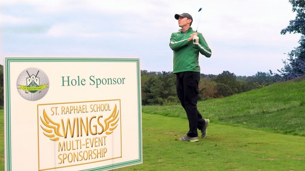 A man playing golf in front of a hole sponsor sign