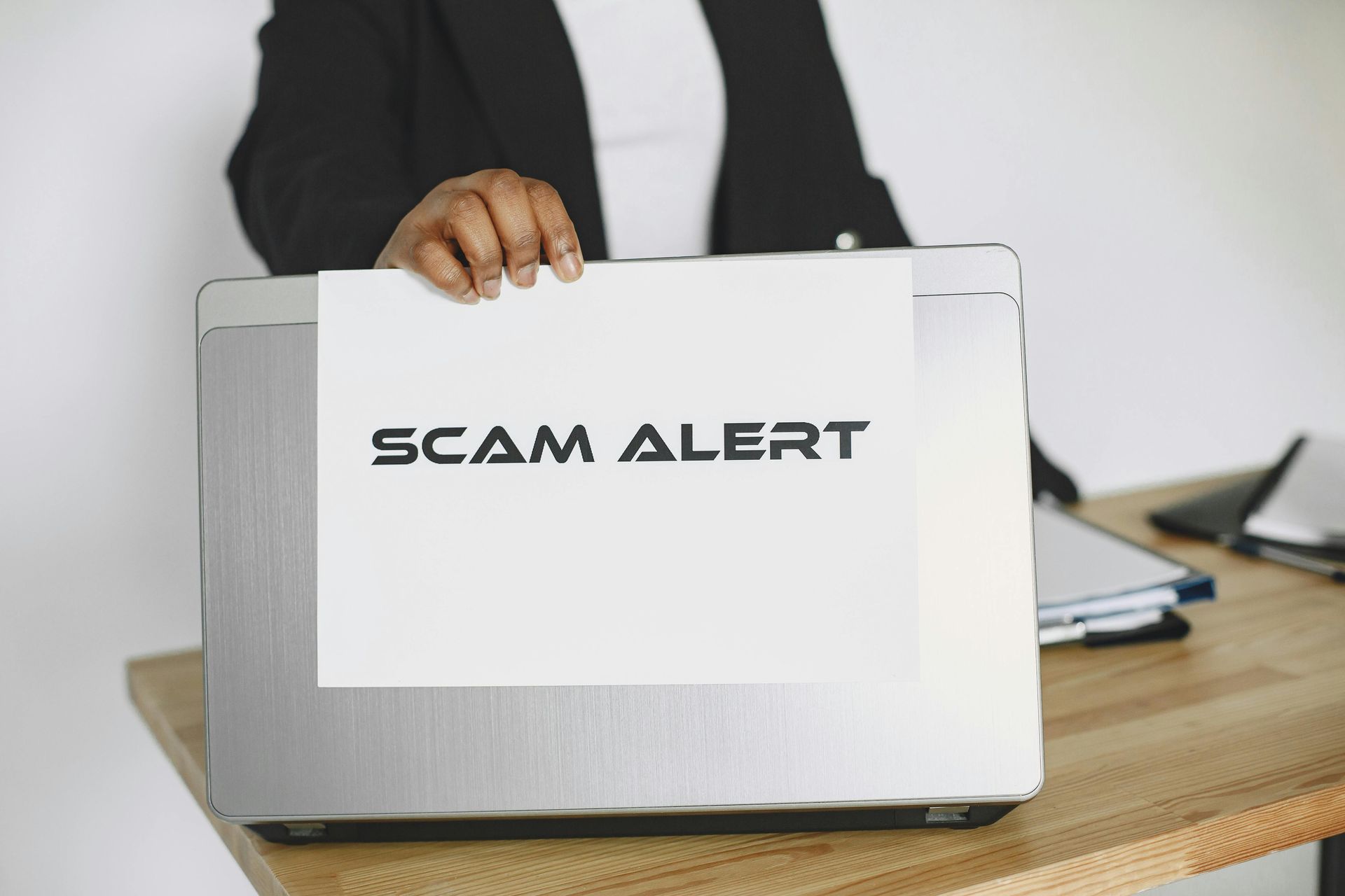 Person holding a gray briefcase labeled “SCAM ALERT” on a desk