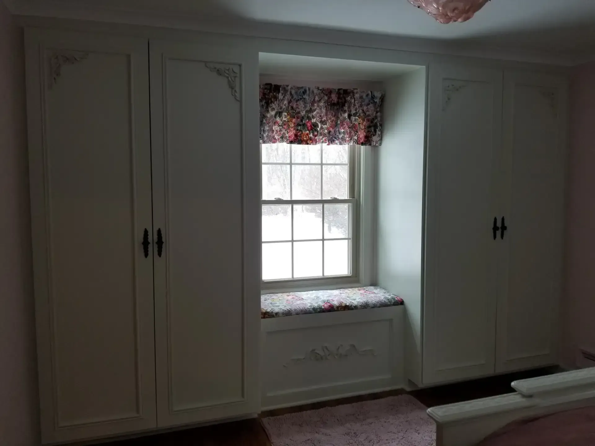 Built-in white cabinets flanking a window with a floral valance and seat cushion. Black hardware.