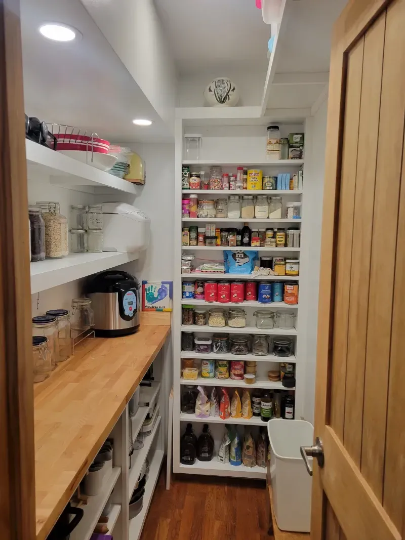 A pantry with white shelves and a wooden countertop filled with food items and storage containers.
