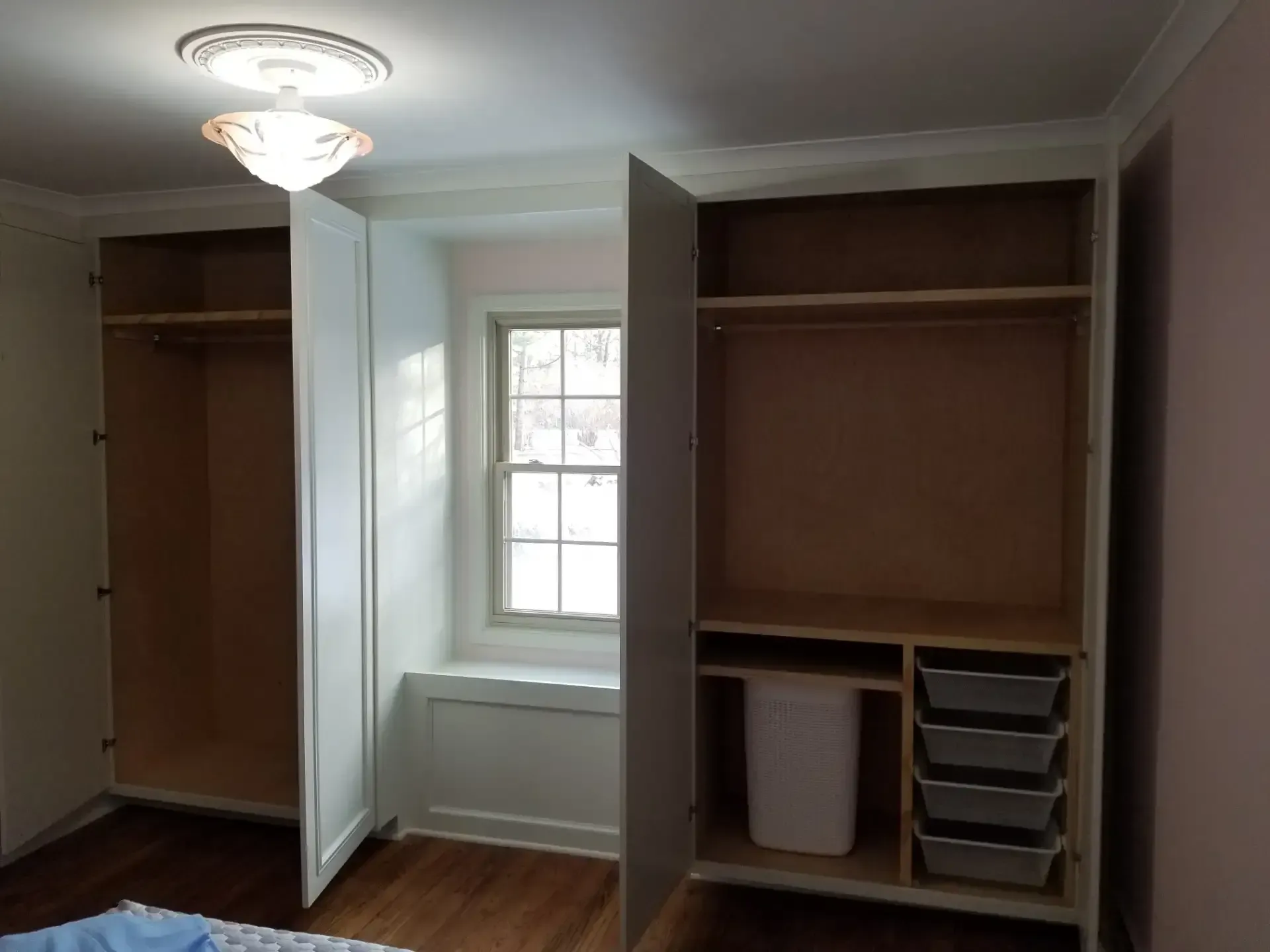 Built-in white closets flanking a window with a bench seat. One closet has hanging rods; the other has drawers.