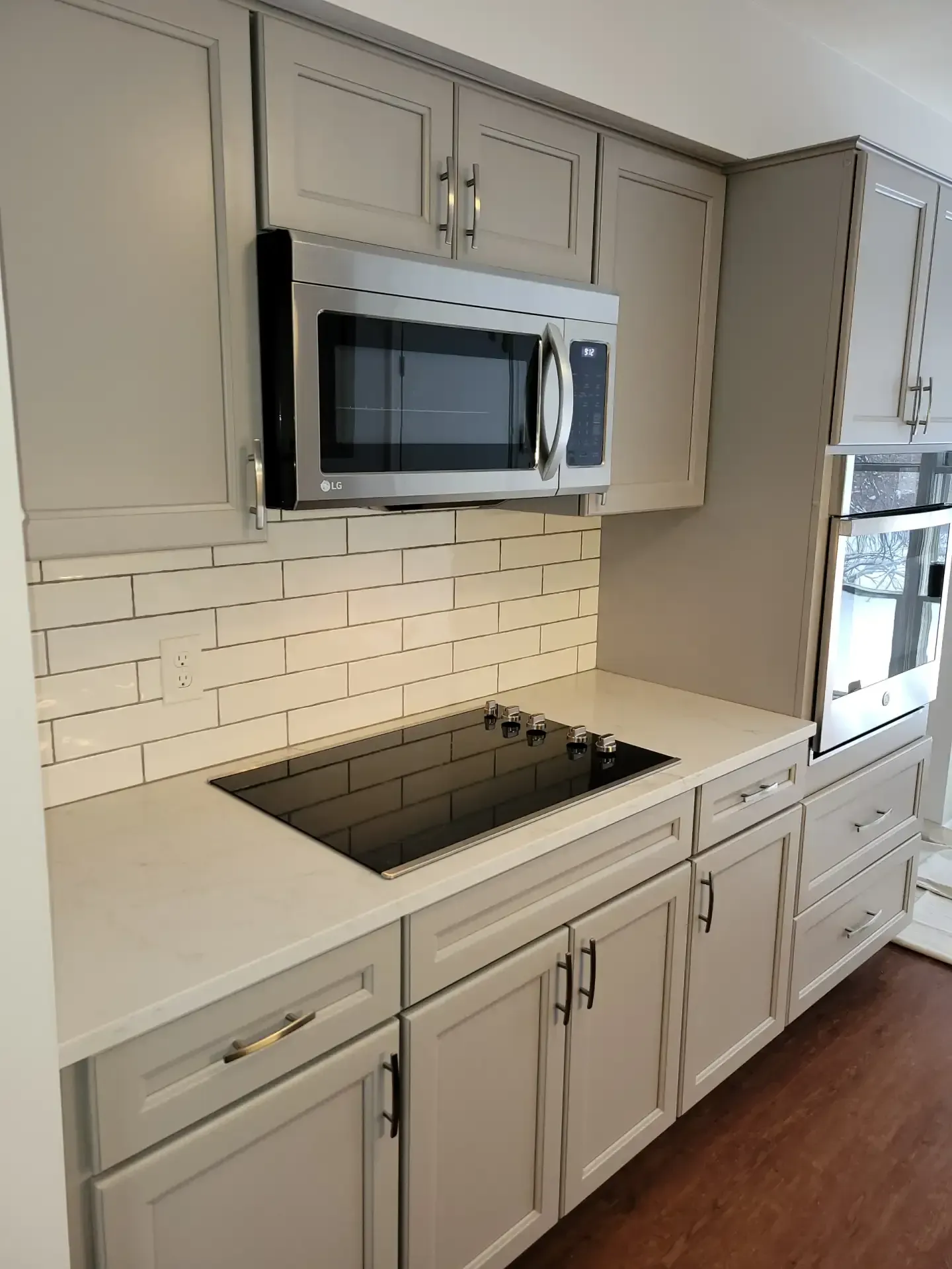 Kitchen with gray cabinets, white countertop, stainless steel microwave, and cooktop.