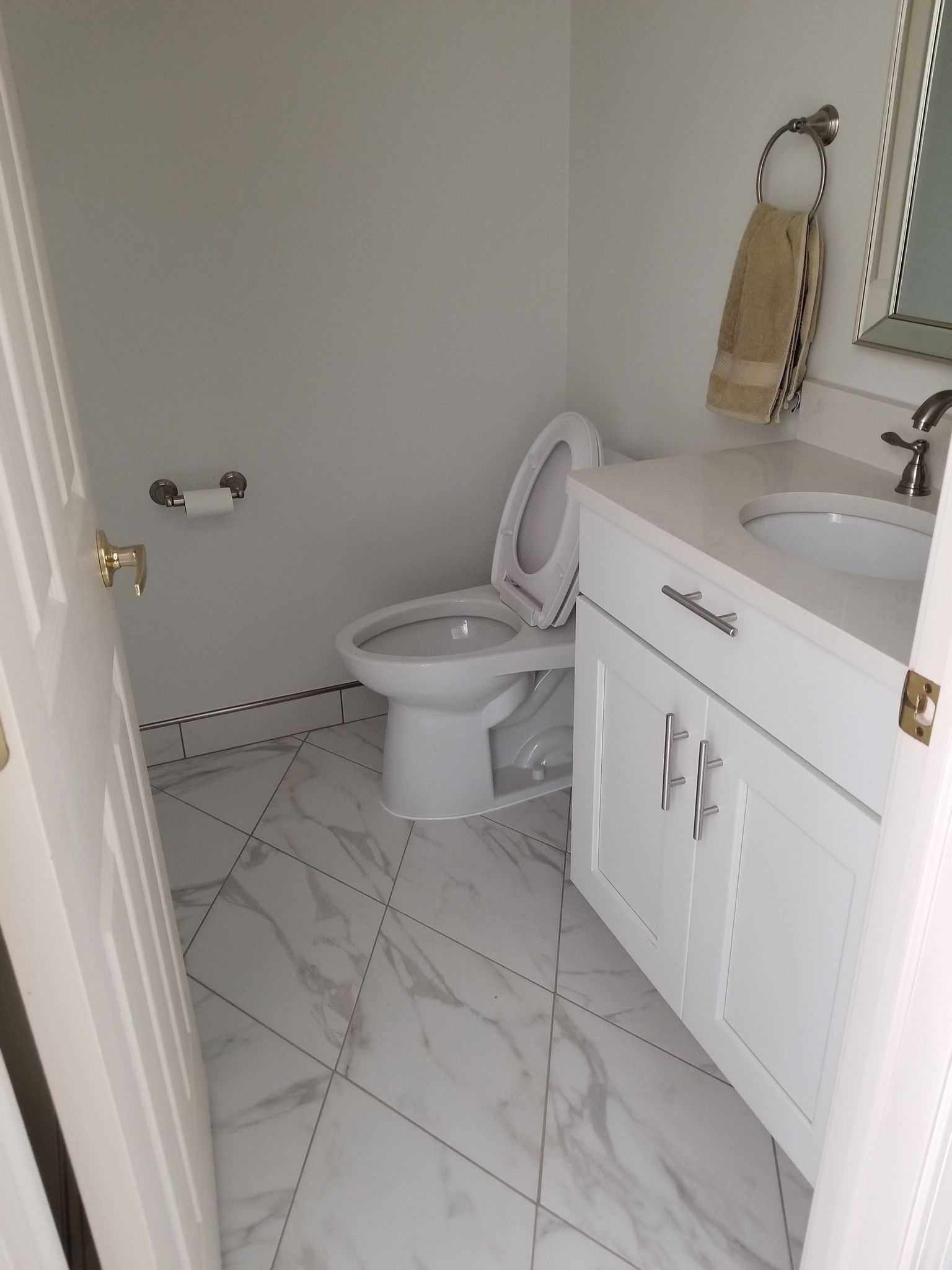A small, white bathroom with a toilet, sink, and marble tile floor.