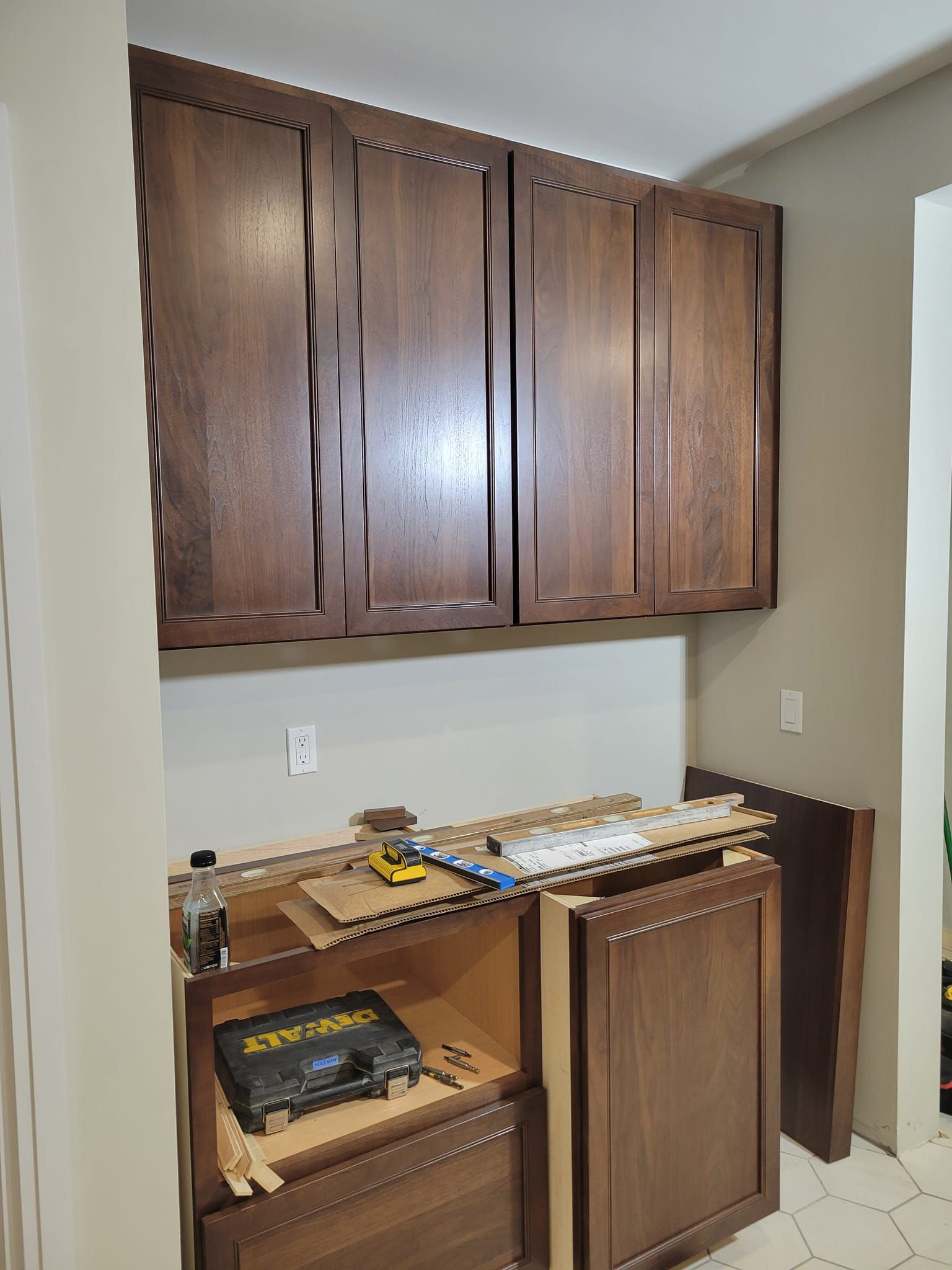 Cabinets under construction: dark wood upper cabinets, lower cabinet doors ajar, tools visible.